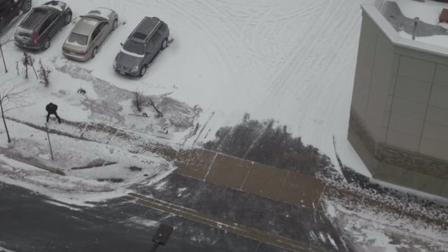 In a heavy snow day of Toronto, a man walks alone beside a parking lot.