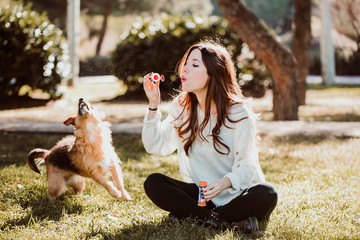 .Pretty young woman playing with her adopted dog sitting on the grass. Throwing soap bubbles....