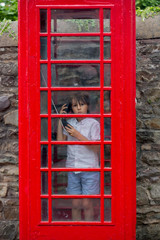 Cute boy, child, calling from a red telephone booth in the city