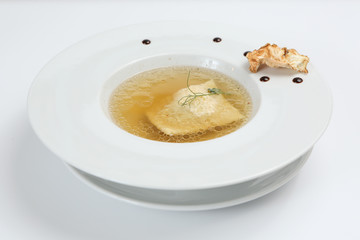 Minimalistic serving of food, white transparent chicken broth in a plate of rice, cheese and dumplings, decorated