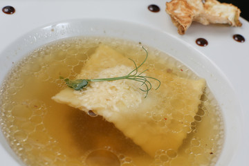 Minimalistic serving of food, white transparent chicken broth in a plate of rice, cheese and dumplings, decorated