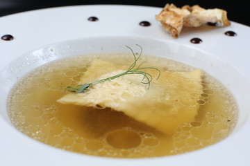 Minimalistic serving of food, white transparent chicken broth in a plate of rice, cheese and dumplings, decorated