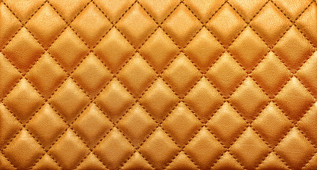 Close-up texture of genuine leather with rhombic stitching. Rich gold color