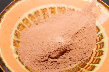 Dry cocoa powder poured into a brown ceramic plate