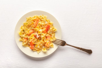 Smoked salmon with bowtie pasta. Farfalle with salmon and a cream sauce, shot from the top on a white linen tablecloth with a fork and a place for text