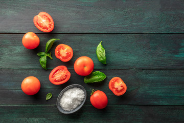 Organic heirloom tomatoes with fresh basil leaves, shot from above on a dark rustic background with...