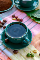 Cup with black coffee served outside with raw green, mature red and roasted coffee beans, decorated with green leaves from coffee plant