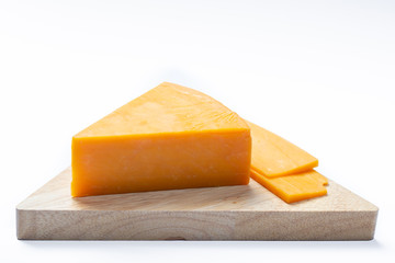 Piece of hard orange Cheddar cheese on wooden cheese plank isolated close up