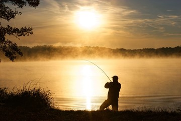Silhouette of angler during misty sunrise