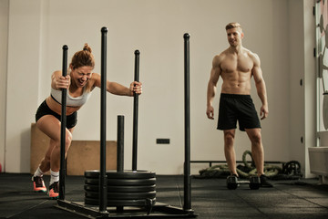 Athletic woman making effort while pushing gym sled with weights on cross training.