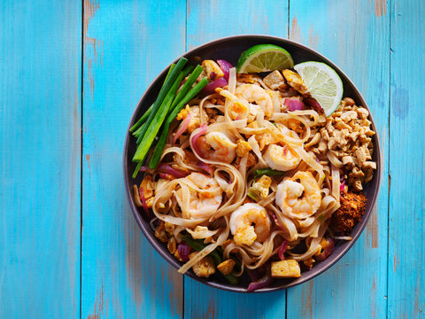 shrimp pad thai on plate in flat lay composition with copy space atop of colorful wooden table