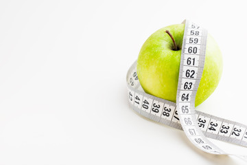 Green apple with tape measure on white desk. Health and diet.