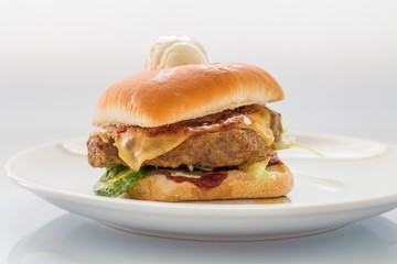 cheeseburger with beef cutlet, bacon, tomatoes and cheese slices, seasoned with sauce and green salad for a restaurant menu on a white isolated background