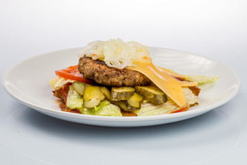 cheeseburger with beef cutlet, bacon, tomatoes and cheese slices, seasoned with sauce and green salad for a restaurant menu on a white isolated background