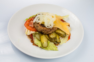 cheeseburger with beef cutlet, bacon, tomatoes and cheese slices, seasoned with sauce and green salad for a restaurant menu on a white isolated background