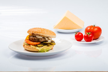 cheeseburger with beef cutlet, bacon, tomatoes and cheese slices, seasoned with sauce and green salad for a restaurant menu on a white isolated background