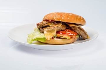 cheeseburger with beef cutlet, bacon, tomatoes and cheese slices, seasoned with sauce and green salad for a restaurant menu on a white isolated background