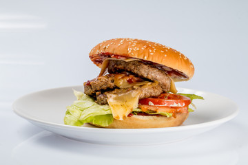 cheeseburger with beef cutlet, bacon, tomatoes and cheese slices, seasoned with sauce and green salad for a restaurant menu on a white isolated background