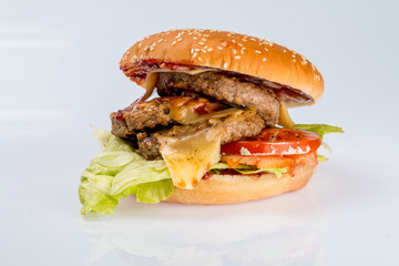 cheeseburger with beef cutlet, bacon, tomatoes and cheese slices, seasoned with sauce and green salad for a restaurant menu on a white isolated background