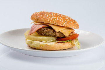 cheeseburger with beef cutlet, bacon, tomatoes and cheese slices, seasoned with sauce and green salad for a restaurant menu on a white isolated background