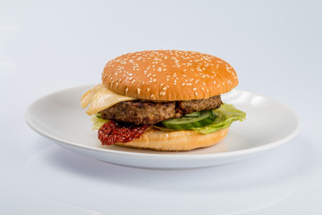 cheeseburger with beef cutlet, bacon, tomatoes and cheese slices, seasoned with sauce and green salad for a restaurant menu on a white isolated background