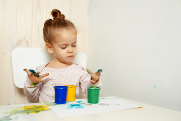 Beautiful little girl draws with finger paints on a white sheet of paper. Creative child development in kindergarten or free time at home