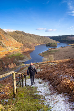 pen y garreg reservoir, Elan Valley Wales. Hiker walking towards lake on a snow covered path looking towards mountains and trees