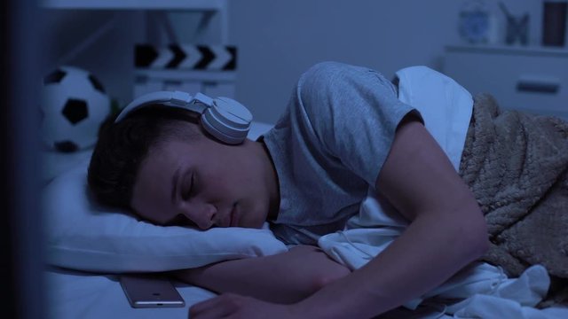 Male teenage boy fallen asleep in headphones, overworked student relaxing