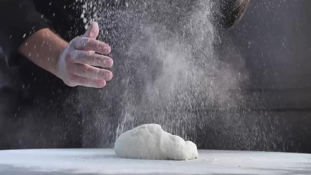 Professional and Skilled Confectioner Adding Ingredients For Preparation Of Dough, Baking Cake. Baker Hand Throwing Flour black shirt white table. pro lighting Master chef style. slow motion