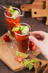 Two glasses of tomato juice decorated with fresh tomatoes, cucumber and leaves on a wooden background