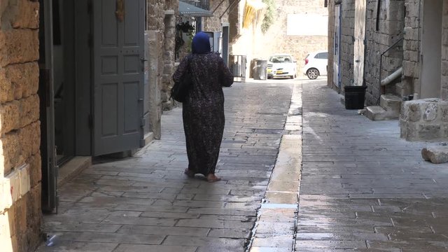 Unrecognizable elder Arab woman walking on the street of Acre, Israel. Rear view