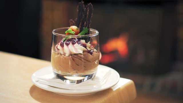 Gourmet dessert of chocolate mousse displayed in a cocktail glass with a fireplace in the background