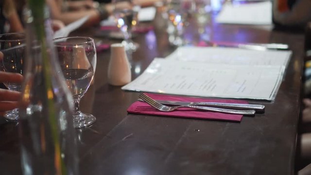 Plastic menus being turned on table set with silverware and pink napkins
