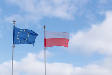 European and Poland flags next to each other waving in the wind against blue sky with clouds