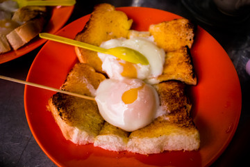 Two half boiled eggs with toast, a famous breakfast among Chineses in Malaysia. Shot in the morning with a warm tone and orange plate as background.