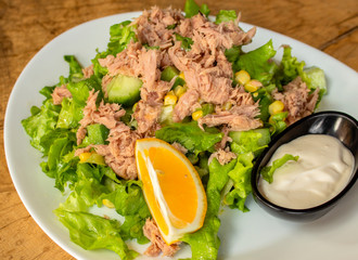 Green salad with tuna. Fresh lettuce, cucumbers, corn, mayonnaise dressing and lemon slice. Closeup.