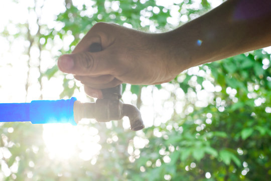 Hand off water valve with blur background of green nature, water saving concept, Hand close water valve to stop water drop from faucet, Energy conservative, Beautiful flare light in the morning