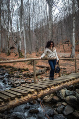 Woman stands on small wooden bridge on creek in the forest