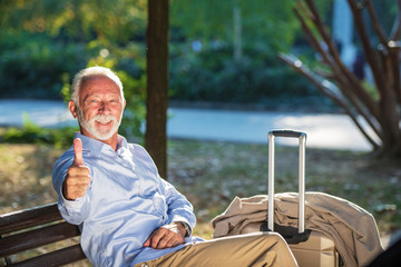 Senior gentleman sitting on a wooden bench and relaxing in a park