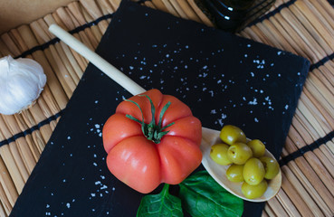 fresh raf tomatoe on a slate dish. garlic, salt olive oil and olves on a wood spoon. Mediterranean diet. Gourmet experience