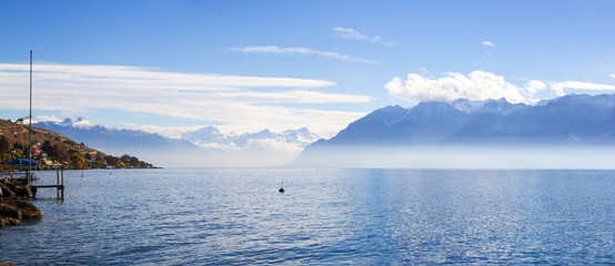 Panorama of Lake Leman or Lake of Geneva with morning mist over the water surface. At the background are the snow-covered Alps, at the right side is mountains in France. - Powered by Adobe