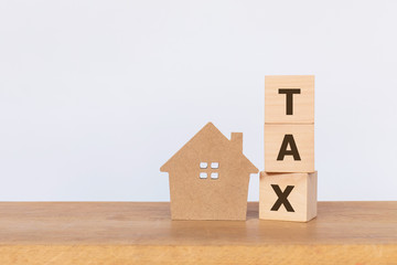 House model and wooden cubes with alphabet TAX on wooden table. Home taxes decrease concept