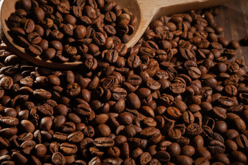 Scattered coffee beans with wooden spoons on wooden table.