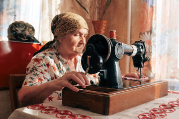 Closeup portrait of old woman using sewing machine, 70 years seamstress working at home