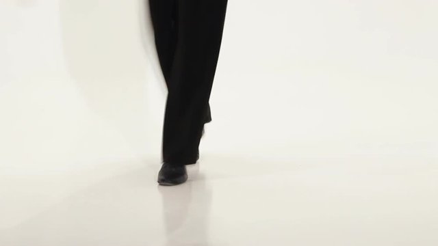 Feets of dancer on the white background who perform graceful movements. Man dancing ballroom dancing in the cyclorama. Black shoes and black pants on the legs