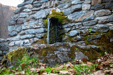 Old stone drinking fountain in the forest. End of winter and beginning of the spring