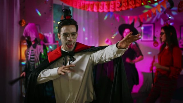 Halloween Costume Party: Count Dracula wearing His Cape Does Doing Vampire Dance, In the Background Beautiful Witch, Gorgeous She Devil and Scary Death and Zombie Dancing in the Decorated Room