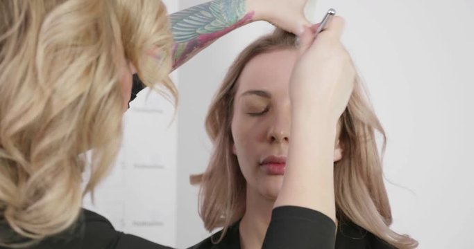 Beauty salon master working with airbrush. Young blone girl customer. Makeup machine used in beauty industry so skin looks great.