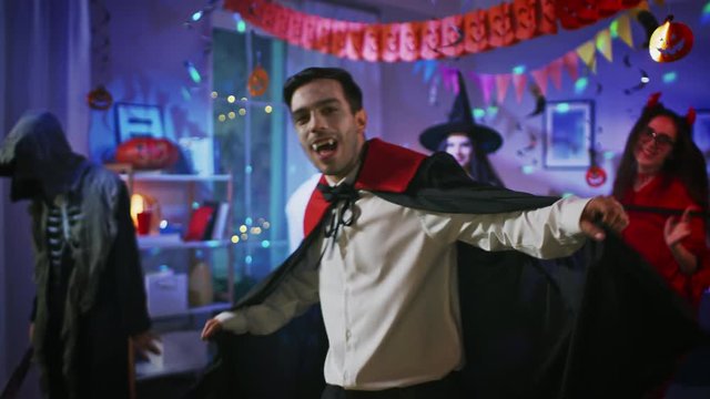 Halloween Costume Party: Count Dracula wearing His Cape Does Doing Vampire Dance, In the Background Beautiful Witch, Gorgeous She Devil and Scary Death and Zombie Dancing in the Decorated Room