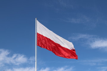 White-red horizontal flag on a flagpole developing in the wind against a blue sky with light clouds. Symbol of the Polish state